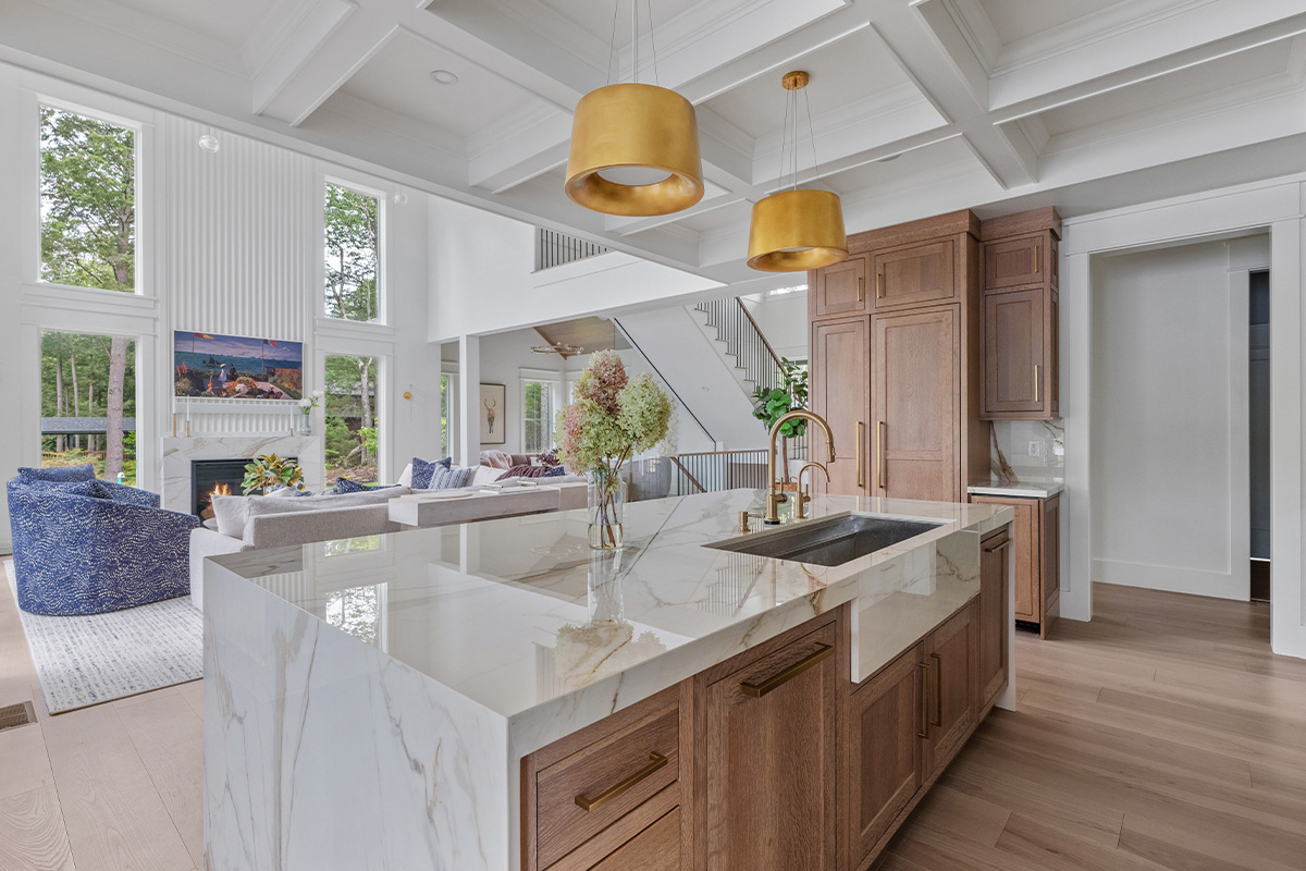 White kitchen cabinets with brown stained island with marble waterfall counter and hood