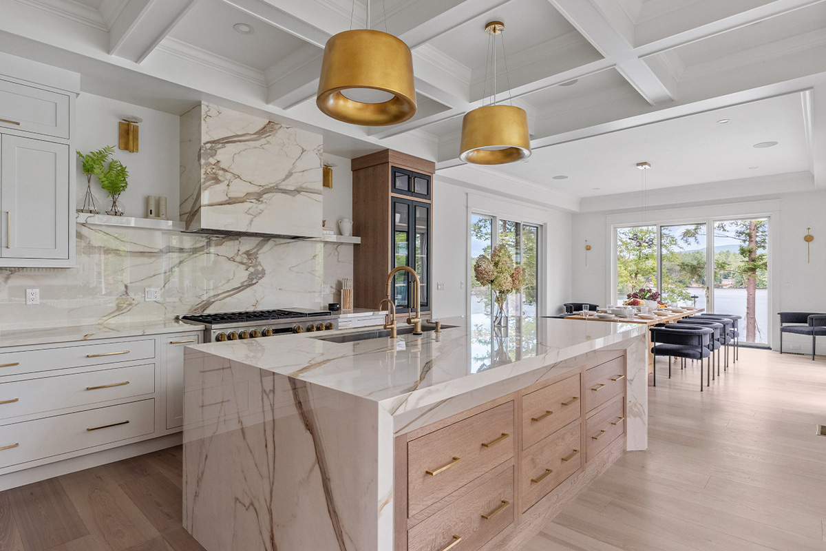White kitchen cabinets with brown stained island with marble waterfall counter and hood