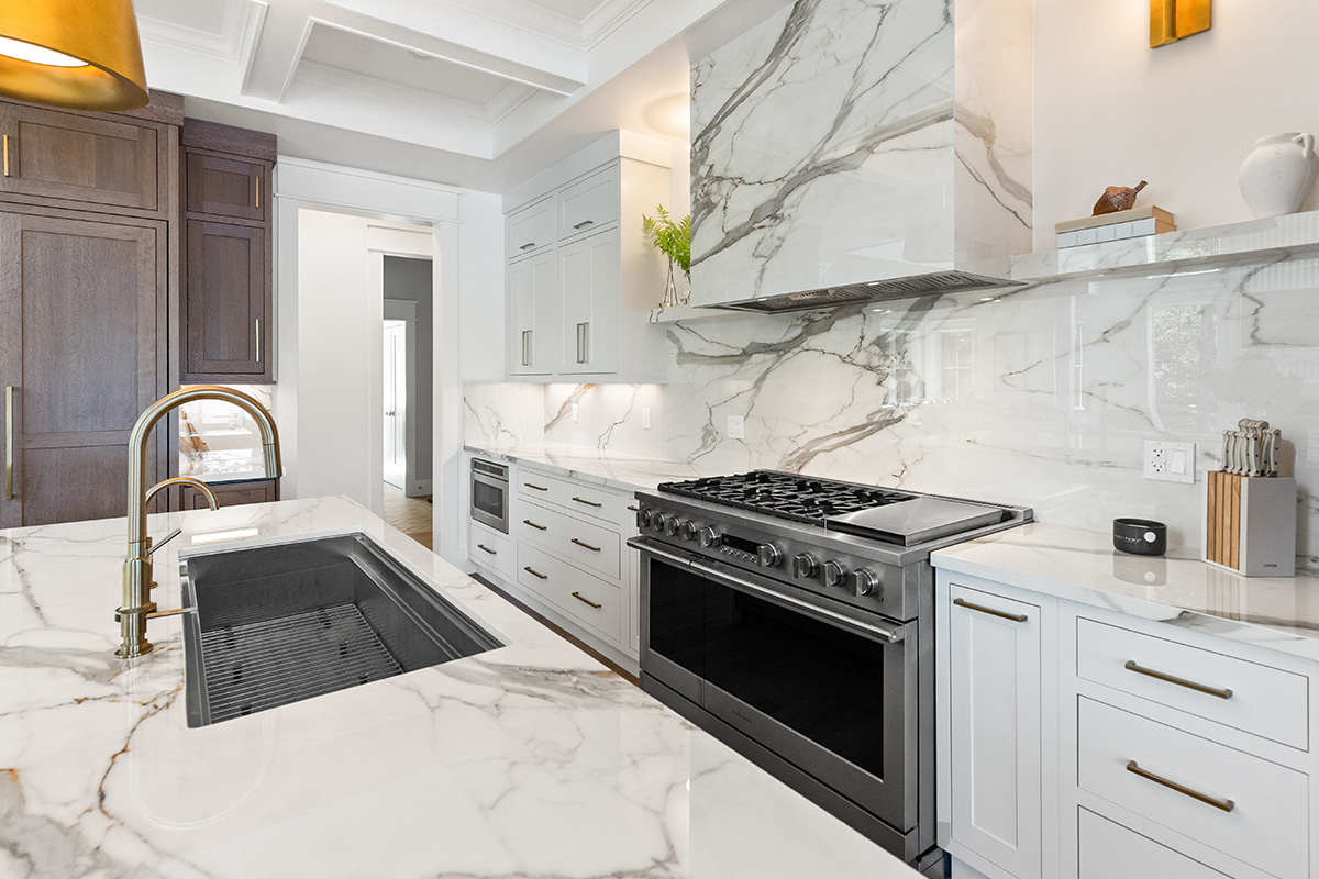 White kitchen cabinets with brown stained island with marble waterfall counter and hood