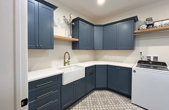 Blue painted laundry room cabinets with white appliances and stained floating shelves