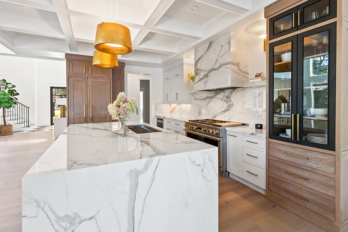 White kitchen cabinets with brown stained island with marble waterfall counter and hood