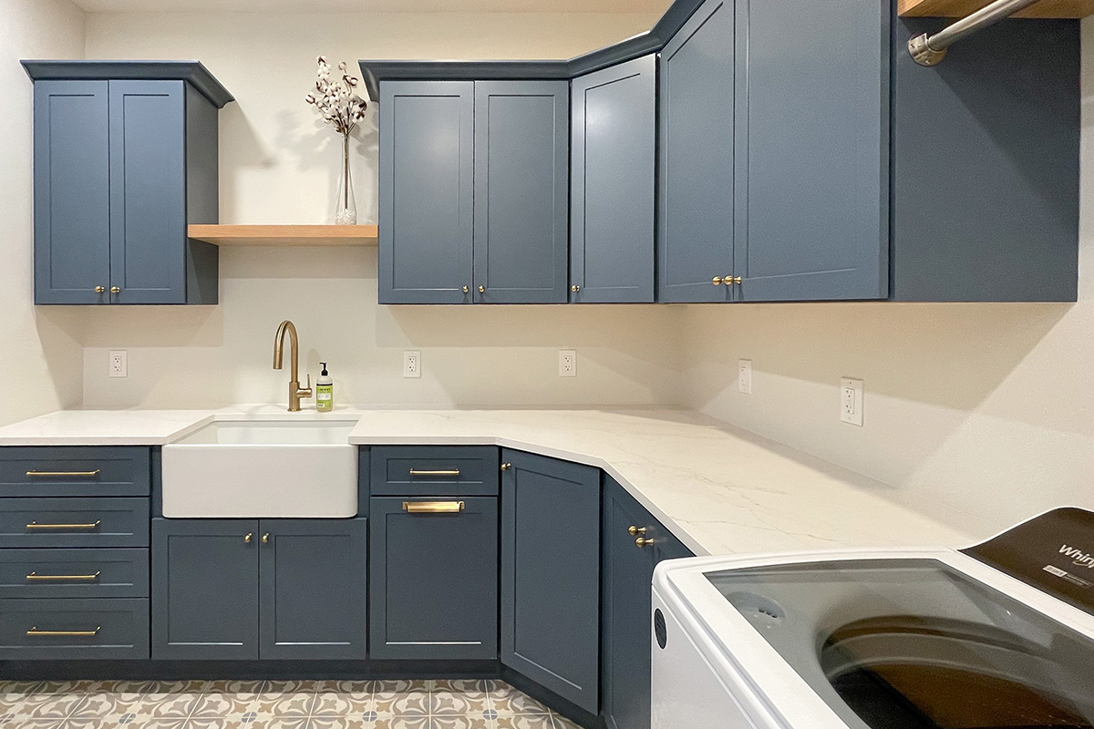 Blue painted laundry room cabinets with white appliances and stained floating shelves