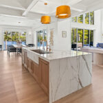 White kitchen cabinets with brown stained island with marble waterfall counter and hood