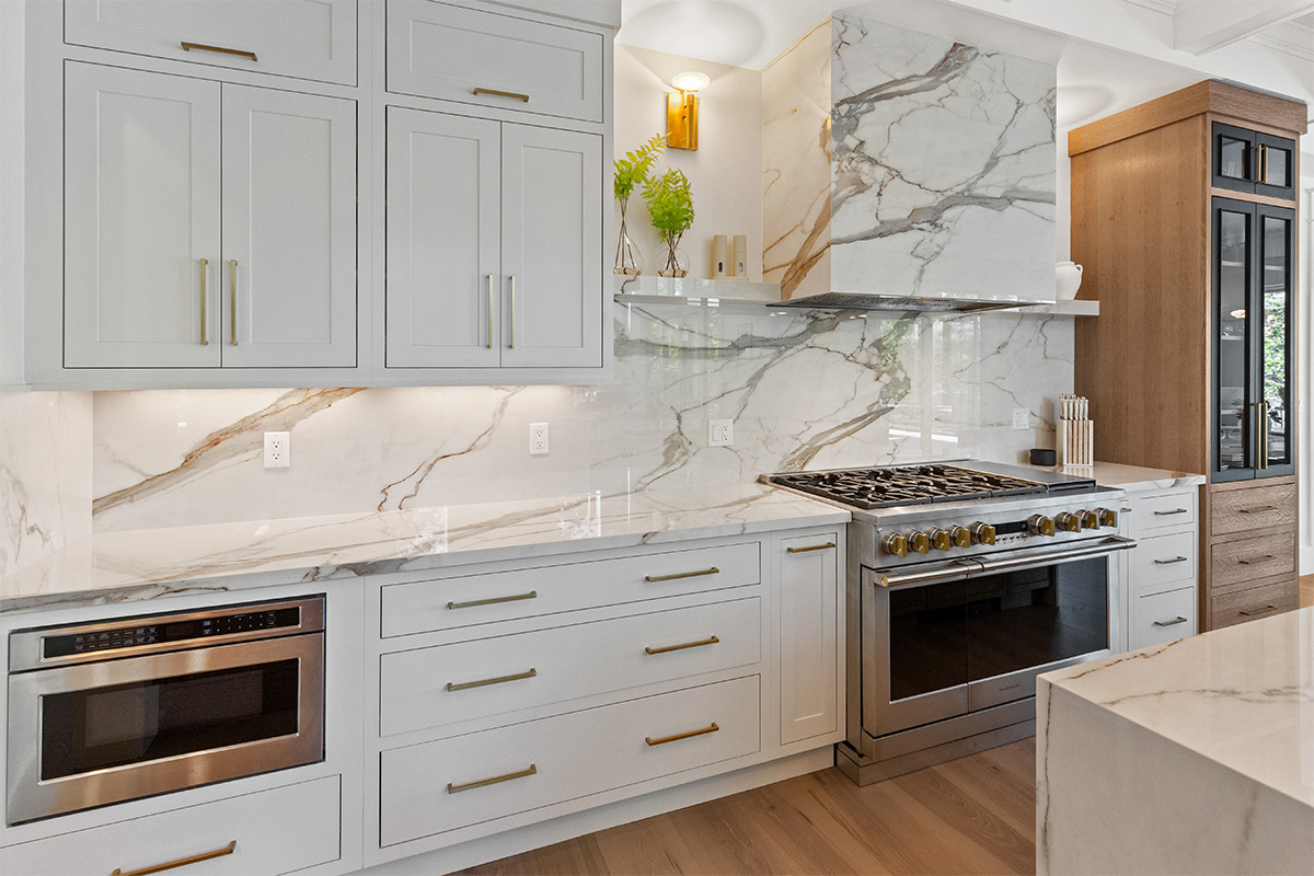 White kitchen cabinets with brown stained island with marble waterfall counter and hood