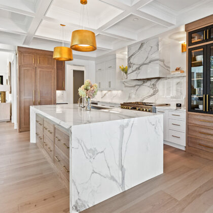 White kitchen cabinets with brown stained island with marble waterfall counter and hood