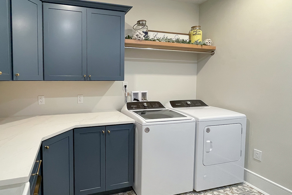 Blue painted laundry room cabinets with white appliances and stained floating shelves