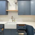Blue painted laundry room cabinets with white appliances and stained floating shelves