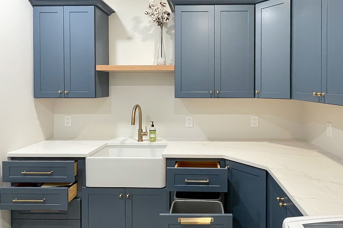 Blue painted laundry room cabinets with white appliances and stained floating shelves