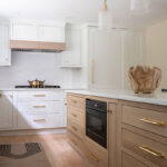 Kitchen with White perimeter cabinets and Quartersawn White Oak island cabinets stained in light brown Pampas finish.