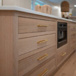 Kitchen with White perimeter cabinets and Quartersawn White Oak island cabinets stained in light brown Pampas finish.