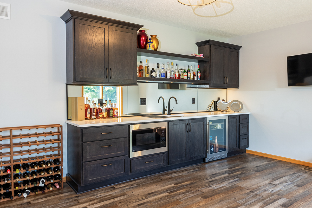 Dark stained bar cabinets with floating shelves, sink, microwave, and wine fridge.