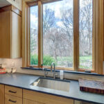 Light brown kitchen sink cabinet with a view out the window above sink.