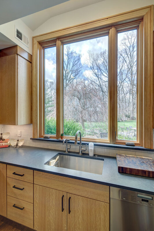 Light brown kitchen sink cabinet with a view out the window above sink.