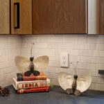 Light brown kitchen cabinet with close up of tile backsplash and items on a counter.
