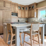 Cashew-stained kitchen perimeter cabinets and gray-painted island with legs and stools.