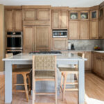 Cashew-stained kitchen perimeter cabinets and gray-painted island with legs and stools.