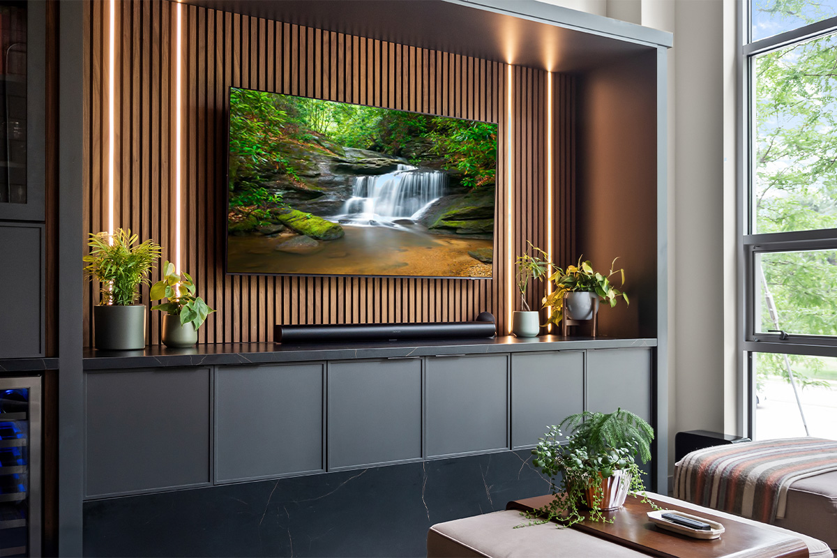 Contemporary entertainment center with gray painted cabinets and stained slatted back wall behind a large mounted tv.