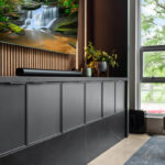 Contemporary entertainment center with gray painted cabinets and stained slatted back wall behind a large mounted tv.