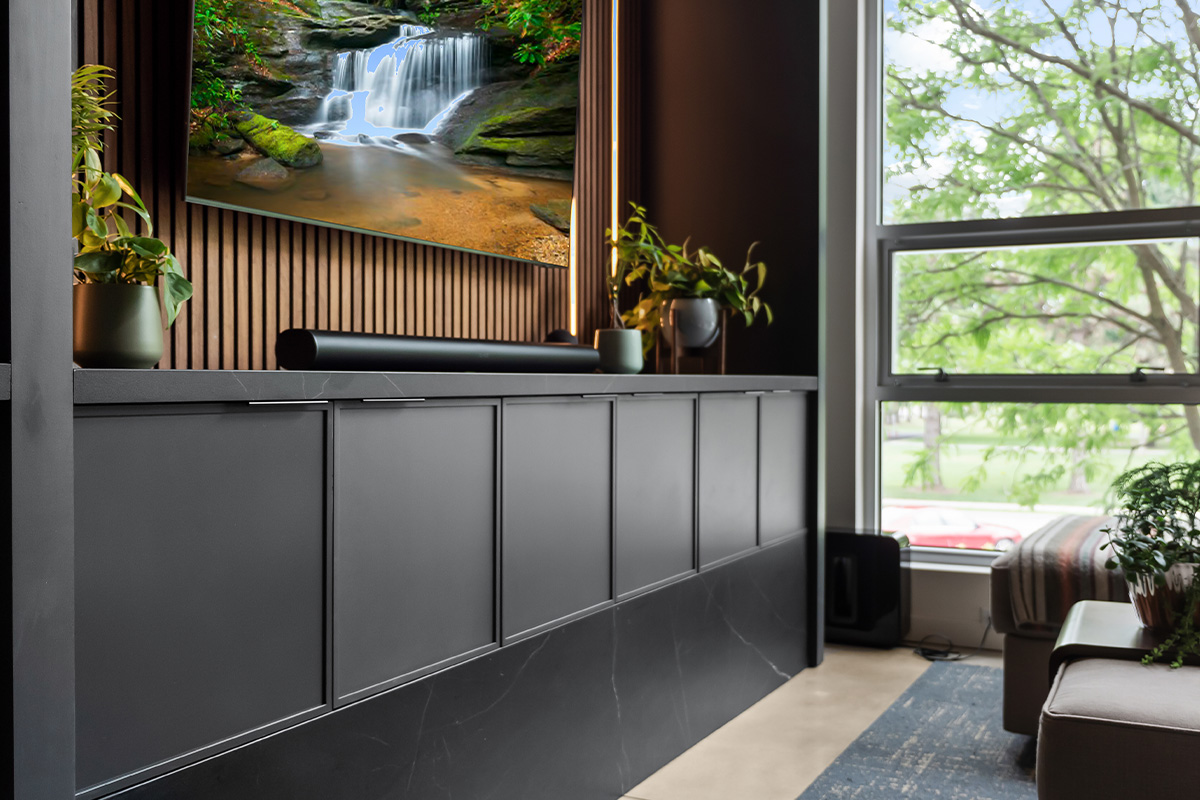 Contemporary entertainment center with gray painted cabinets and stained slatted back wall behind a large mounted tv.