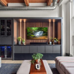 Contemporary entertainment center with gray painted cabinets and stained slatted back wall behind a large mounted tv.