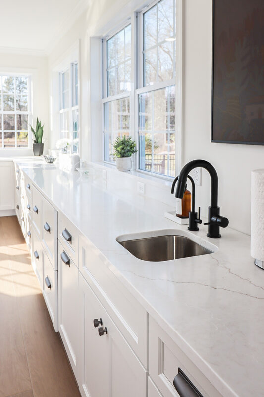 White kitchen cabinets with large row of windows above.