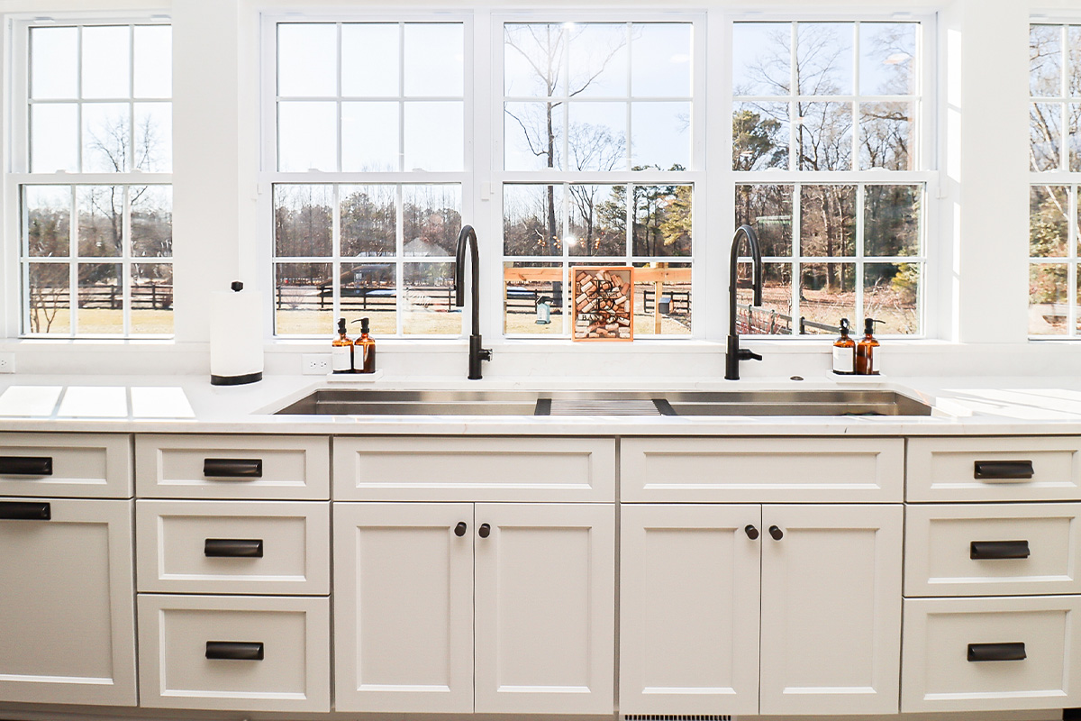 White kitchen cabinets with large row of windows above.