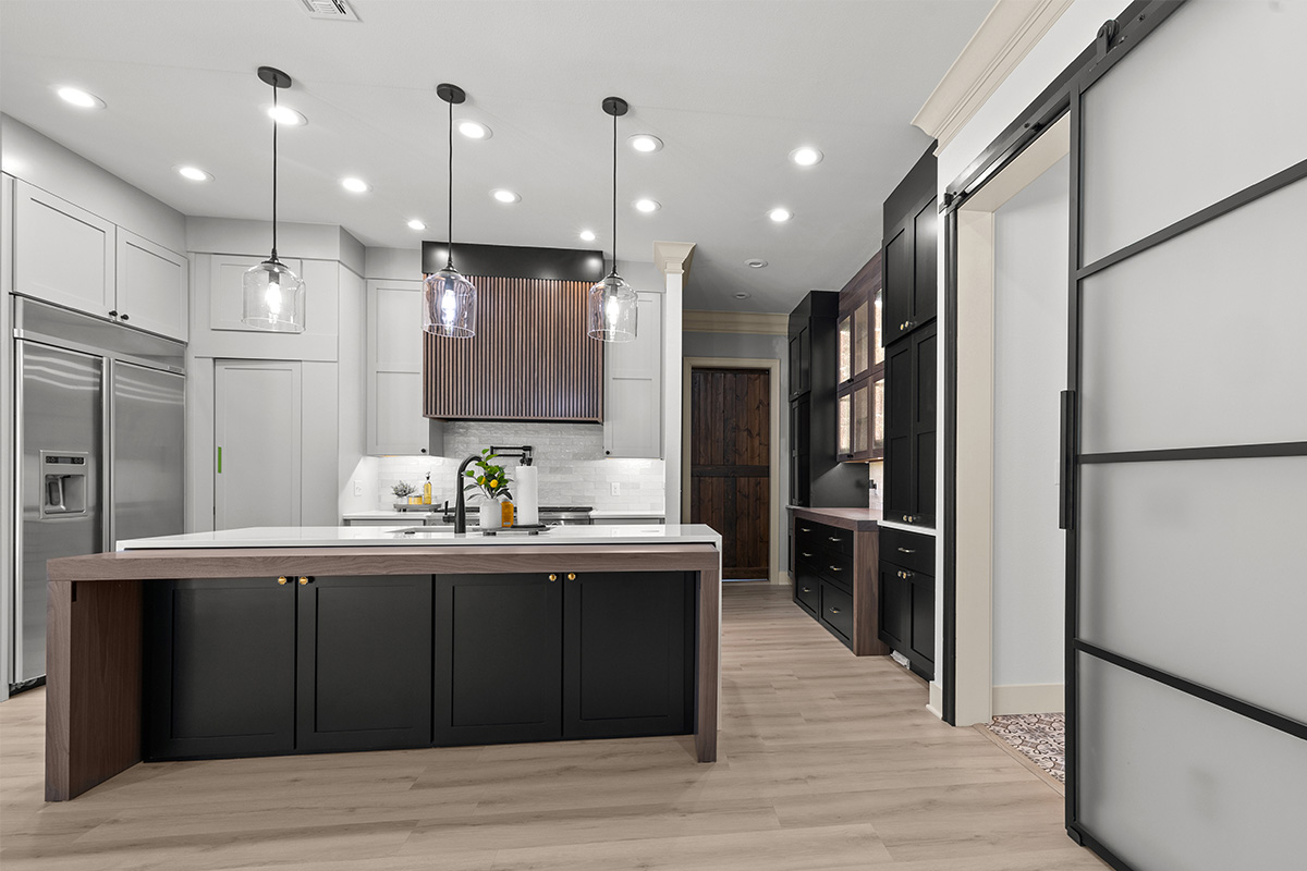 Light gray and black painted kitchen cabinets with walnut accent hutch cabinets, with a pullout walnut table connected to the island.