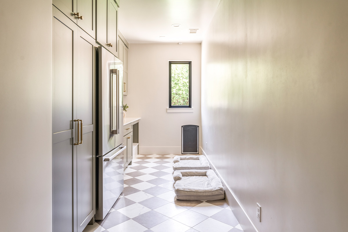 Light green mudroom cabinets with dog dish area under the counter and dog beds on the floor.