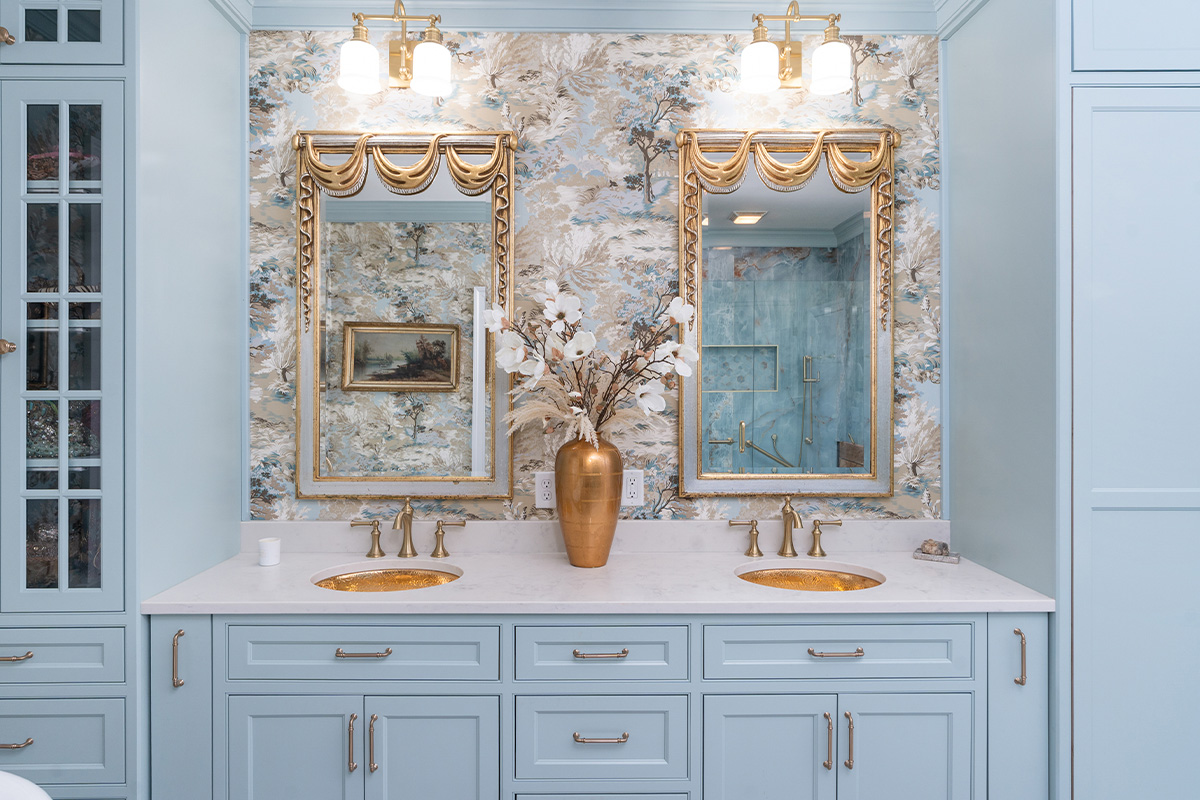 Light blue bathroom vanity cabinets with ornate gold mirrors and sink hardware.