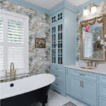 Light blue bathroom vanity cabinets with ornate gold mirrors and sink hardware. Also showing a black standalone tub.