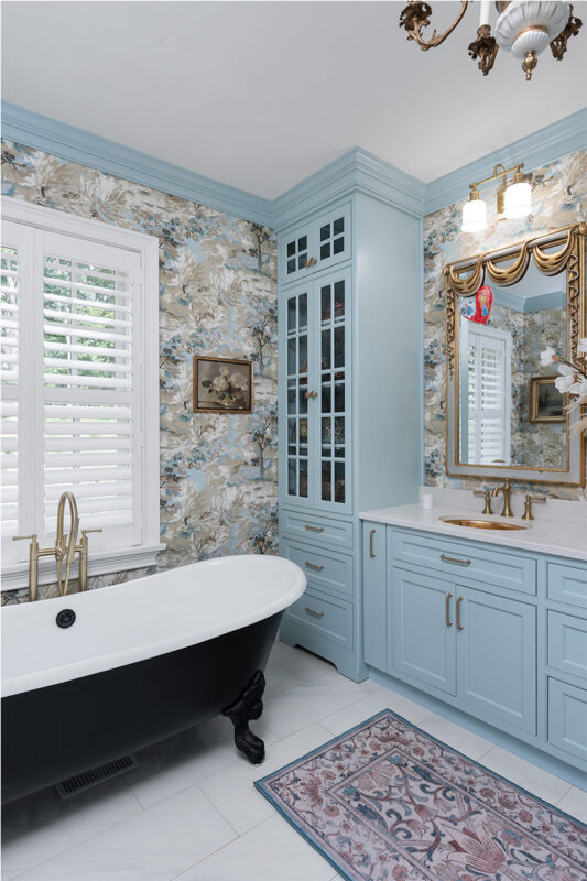 Light blue bathroom vanity cabinets with ornate gold mirrors and sink hardware. Also showing a black standalone tub.
