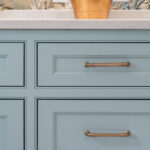 Light blue bathroom vanity cabinets with ornate gold drawer hardware.