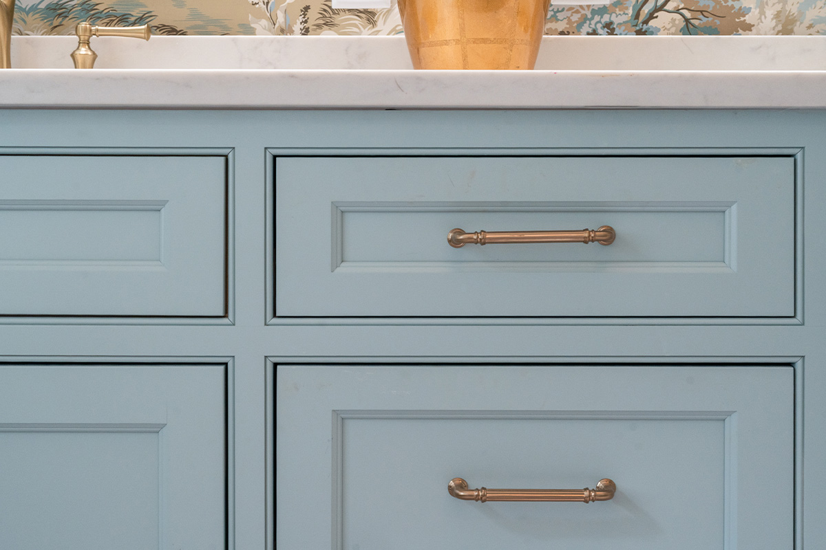 Light blue bathroom vanity cabinets with ornate gold drawer hardware.