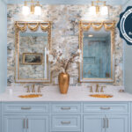 Light blue bathroom vanity cabinets with ornate gold mirrors and sink hardware.