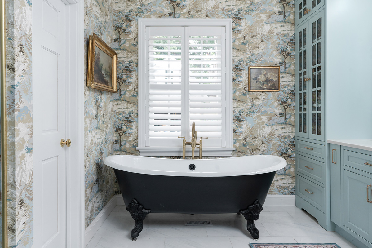 Black standalone tub with flowered wall paper.