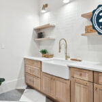 Light stained mudroom cabinets with farmer sink and floating shelves.