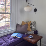 Painted purple window seat cabinet next to a window.