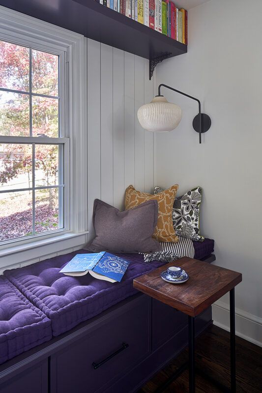 Painted purple window seat cabinet next to a window.
