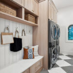 Light stained mudroom locker cabinets with double stacked washer and dryer in the distance.