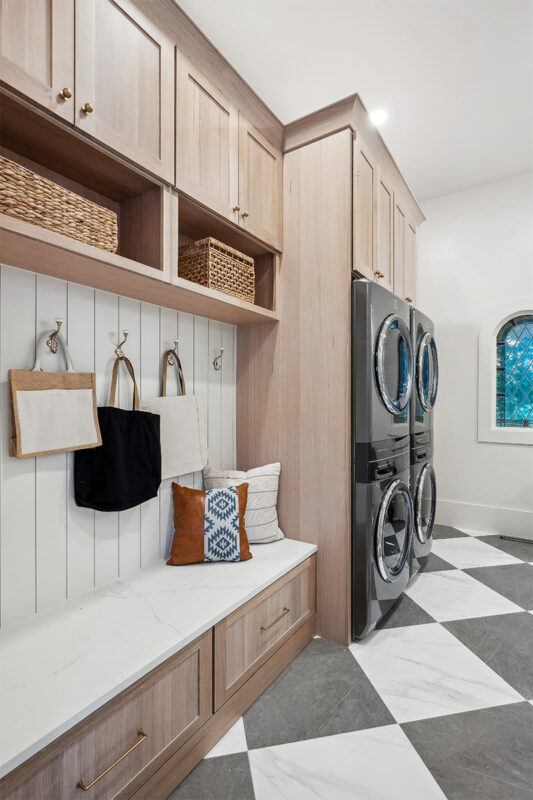 Light stained mudroom locker cabinets with double stacked washer and dryer in the distance.