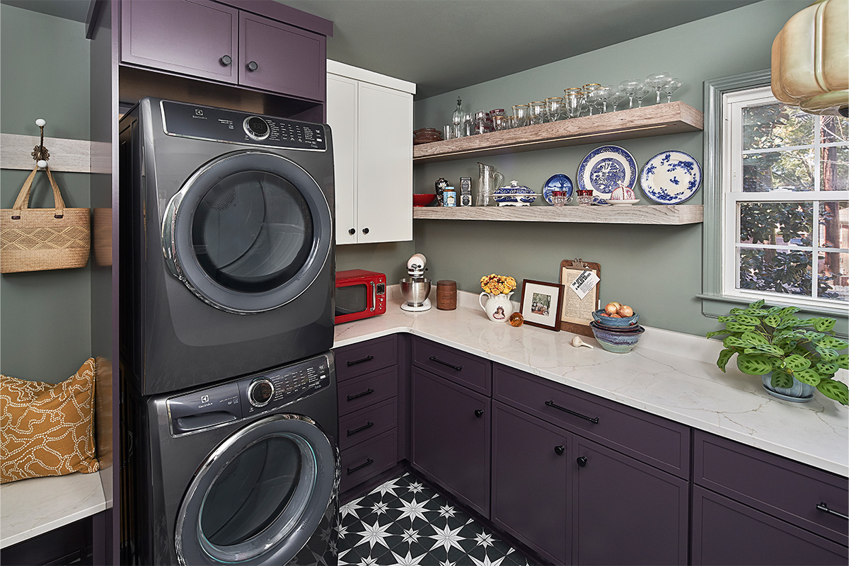 Purple stacked washer and dryer next to purple cabinets with stained wood floating shelves.