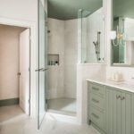 Light green painted bathroom vanity next to a shower with glass door.