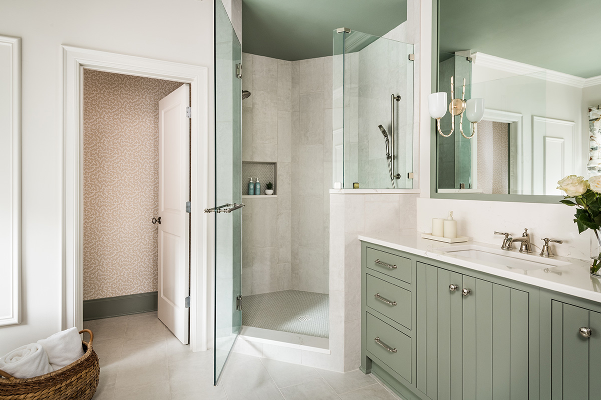 Light green painted bathroom vanity next to a shower with glass door.