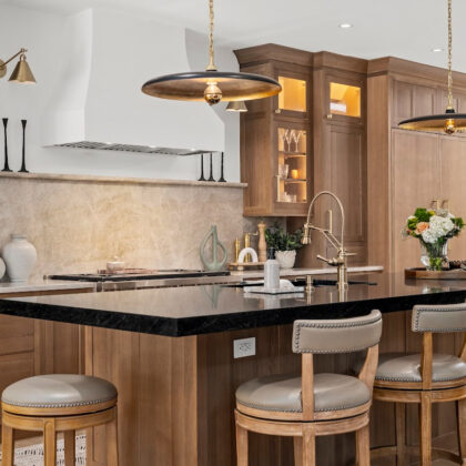 Light brown stained kitchen cabinets with white hood and black counter on island.