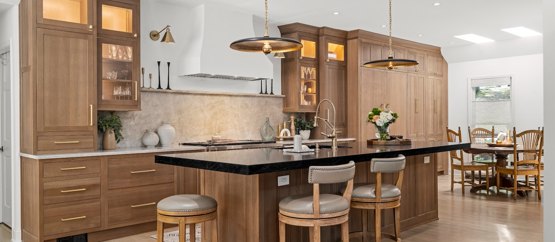 Light brown stained kitchen cabinets with white hood and black counter on island.