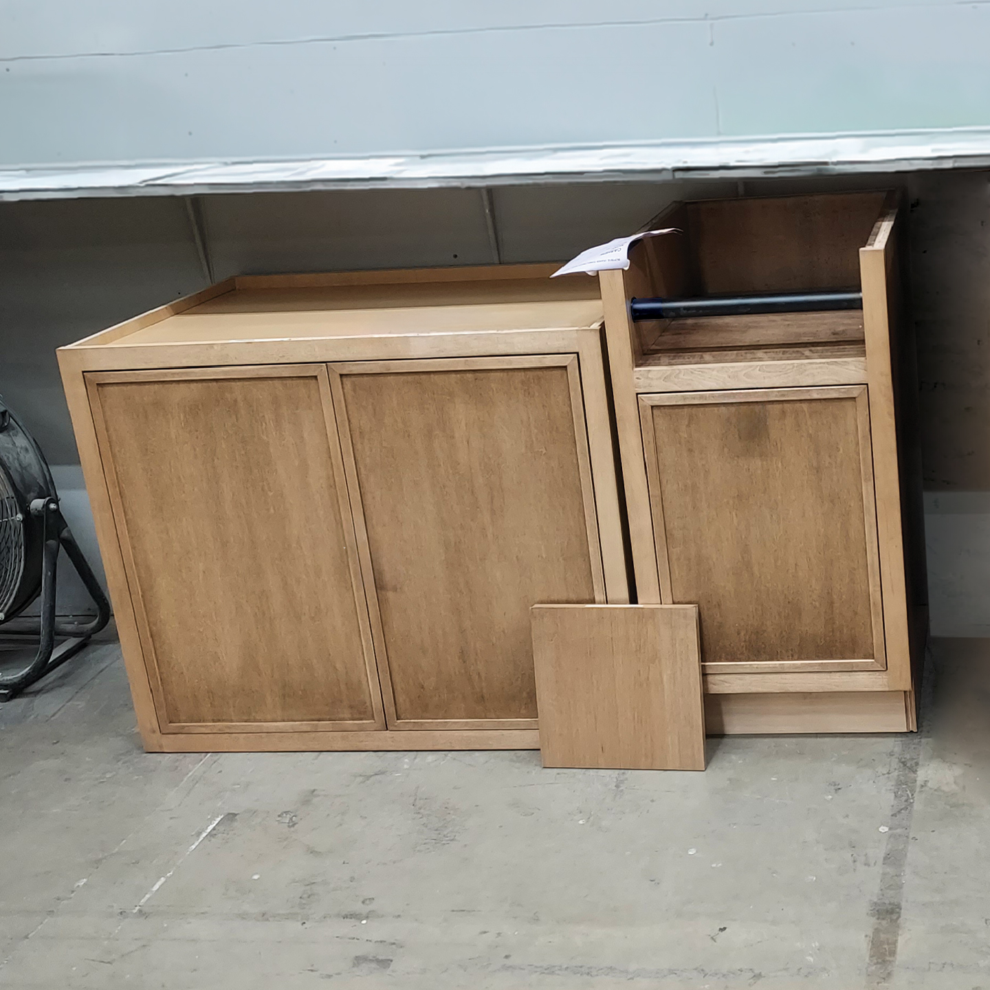 Brown stained wall cabinet and base cabinet with paper towel holder accessory in a warehouse.