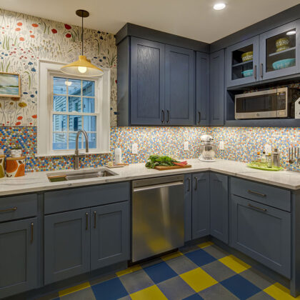 Blue kitchen cabinets with blue and yellow checkered floor and colorful backsplash.