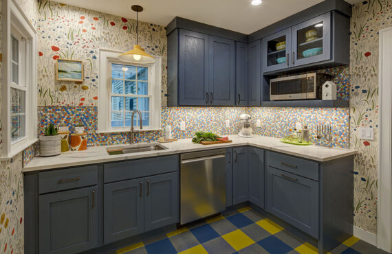 Blue kitchen cabinets with blue and yellow checkered floor and colorful backsplash.