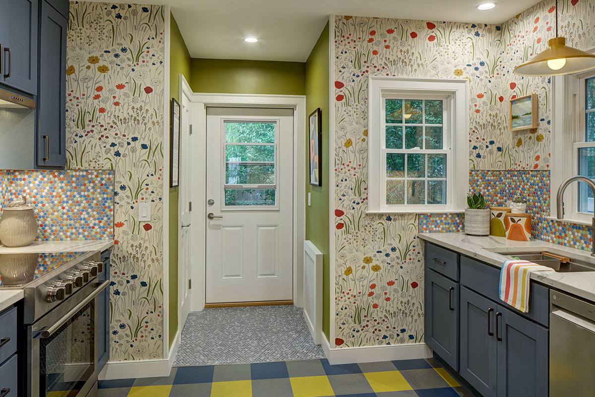Blue kitchen cabinets with blue and yellow checkered floor and colorful backsplash.