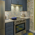 Blue kitchen cabinets with blue and yellow checkered floor and colorful backsplash.